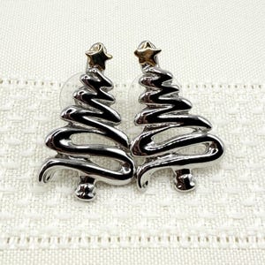 May include: A pair of silver-toned earrings shaped like stylized Christmas trees with a smooth, reflective finish. Each tree features a small, gold-toned star at the very top, adding a subtle contrast to the polished silver metal design.