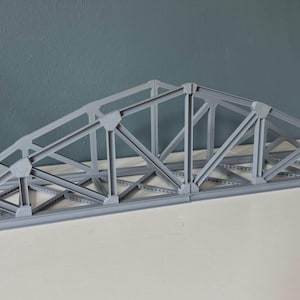 May include: A grey model of a bridge truss, constructed from angled beams and joints. The structure is a representation of a bridge's support system. The model is designed to demonstrate the principles of structural engineering.