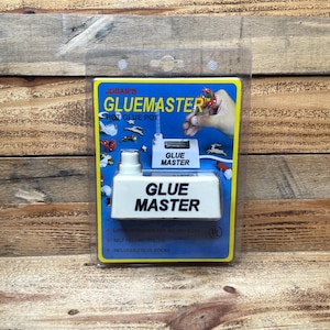 May include: A white Glue Master hot glue pot in clear plastic retail packaging. The blue cardboard backing features the text Jobar's Gluemaster, a graphic of a hand using the tool, and a list of features including a large reservoir and self-feeding system.