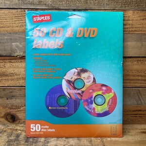 May include: A package of Staples 50 CD & DVD matte disc labels. The package is teal and orange, with the Staples logo in the upper left corner. The package includes three CD designs with the words "Vacation", "Harmon Investments", and "Dance All Night Mix".