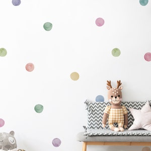 Può includere: Un muro bianco con pois colorati in acquerello, una panca grigia con un cuscino a motivi chevron grigi e bianchi, un giocattolo di cervo di peluche seduto sulla panca e un cesto di vimini con un animale di peluche grigio e bianco.