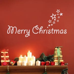 Può includere: Un adesivo da parete bianco con il testo Merry Christmas in corsivo e un gruppo di stelle sopra. L'adesivo è applicato su una parete rossa sopra una mensola del camino in legno decorata con candele, regali incartati e calze natalizie.