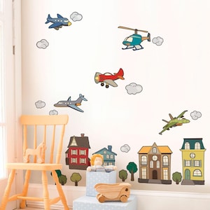May include: A collection of wall decals depicting cartoon aeroplanes, a helicopter, clouds, and houses. The decals are in various colours, including red, blue, green, and yellow. A wooden chair, a toy horse, and a wooden truck are also visible.