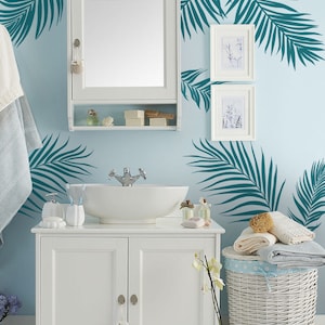Peut inclure: Vasque de salle de bain blanc avec un lavabo en porcelaine blanche et un robinet chrom&eacute;. Le meuble sous vasque a deux portes avec des boutons argent&eacute;s. Un panier &agrave; linge en osier blanc avec un motif &agrave; pois bleus et blancs se trouve &agrave; droite du meuble sous vasque. Le mur derri&egrave;re le meuble sous vasque est bleu clair et comporte des autocollants en forme de feuilles de palmier turquoise.