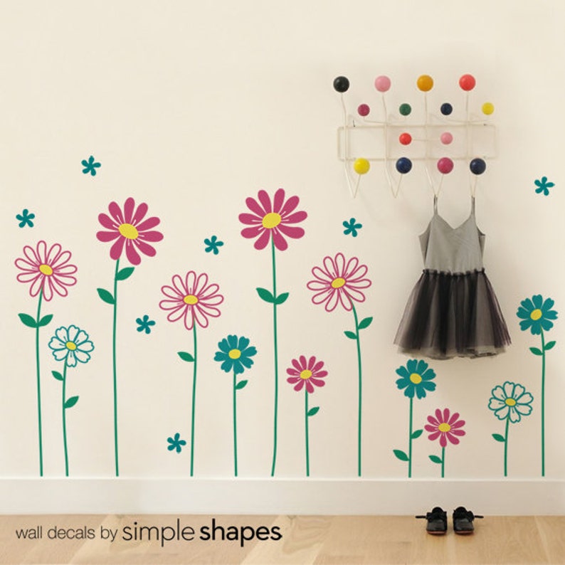 May include: Wall decals featuring a row of colorful flowers with green stems and white, pink, and blue petals. The decals are on a white wall with a wooden floor.