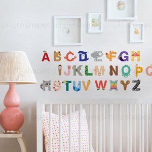 May include: Colorful alphabet wall decals with animal and object illustrations. The letters are in various colors and feature designs like a bear, crab, dolphin, and zebra. The wall art is displayed in a nursery setting.