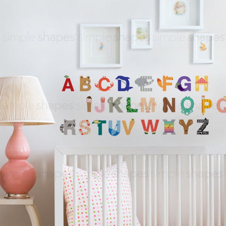May include: Colorful alphabet wall decals with animal and object illustrations. The letters are in various colors and feature designs like a bear, crab, dolphin, and zebra. The wall art is displayed in a nursery setting.
