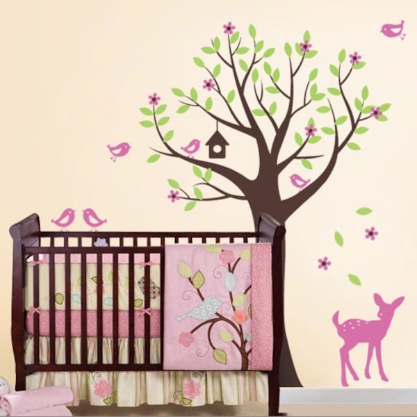 May include: A dark wood crib with a pink and green patterned quilt featuring a bird and tree design. The wall behind the crib displays a large brown tree wall decal with light green leaves, pink flowers, a birdhouse, and pink birds.