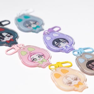 May include: A collection of colorful acrylic keychains featuring anime-style characters in animal-themed outfits. Each keychain has a different color scheme, including pink, blue, and yellow, with matching clasp hardware.