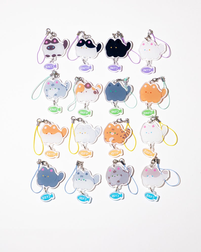 May include: A collection of cat-shaped keychains in various colors and patterns. Each keychain has a different personality type abbreviation, such as ENTJ or INFP, on a small fish-shaped tag. The keychains are attached to a metal clasp with a colorful lanyard.