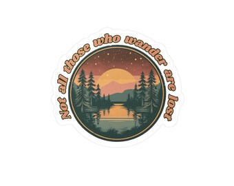 Peut inclure: Autocollant rond avec un paysage de lac, de montagnes et de pins au coucher du soleil. Le texte "Not all those who wander are lost" est disposé en cercle. La palette de couleurs comprend des tons orange, vert et marron.