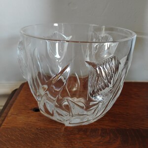 May include: A clear glass bowl with a tulip design. The bowl has a rounded shape with a wide opening and is made of clear glass. The tulip design is etched into the glass, adding a decorative element. The bowl sits on a wooden surface.