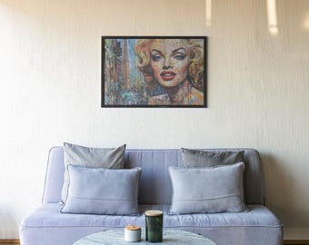 May include: A light grey sofa with a black frame and three grey throw pillows. A framed print of a woman's face with a colourful background hangs on the wall above the sofa. A small round table with a grey surface sits in front of the sofa.