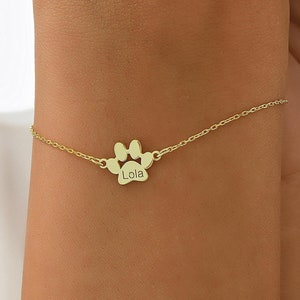 May include: Gold paw print charm bracelet with the name "Lola" engraved on the charm.