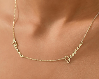 May include: A gold-coloured necklace with two names in a cursive font: "Teresa" and "Jessica." The necklace is worn around the neck, with the names positioned on the chest. The chain is thin and elegant, suitable for everyday wear.