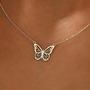 Könnte beinhalten: Eine zarte goldene Kettenkette mit einem ausgeschnittenen Schmetterlingsanhänger.