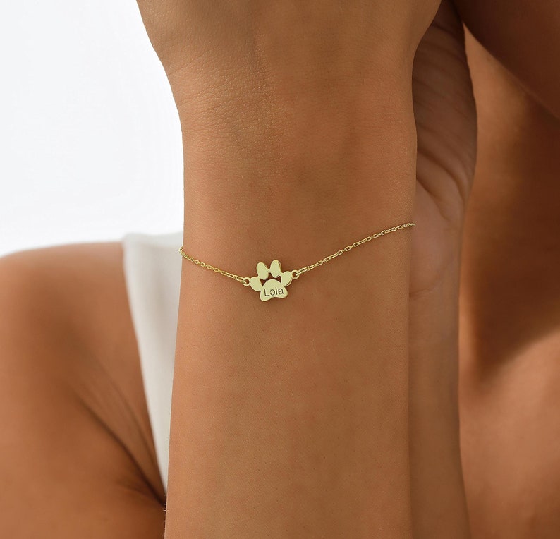 May include: Gold paw print charm bracelet with the name "Lola" engraved on the charm.