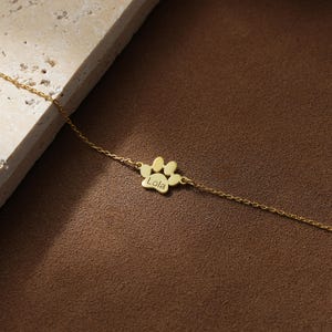 May include: A gold chain necklace with a paw print charm that says "Lola" on it.