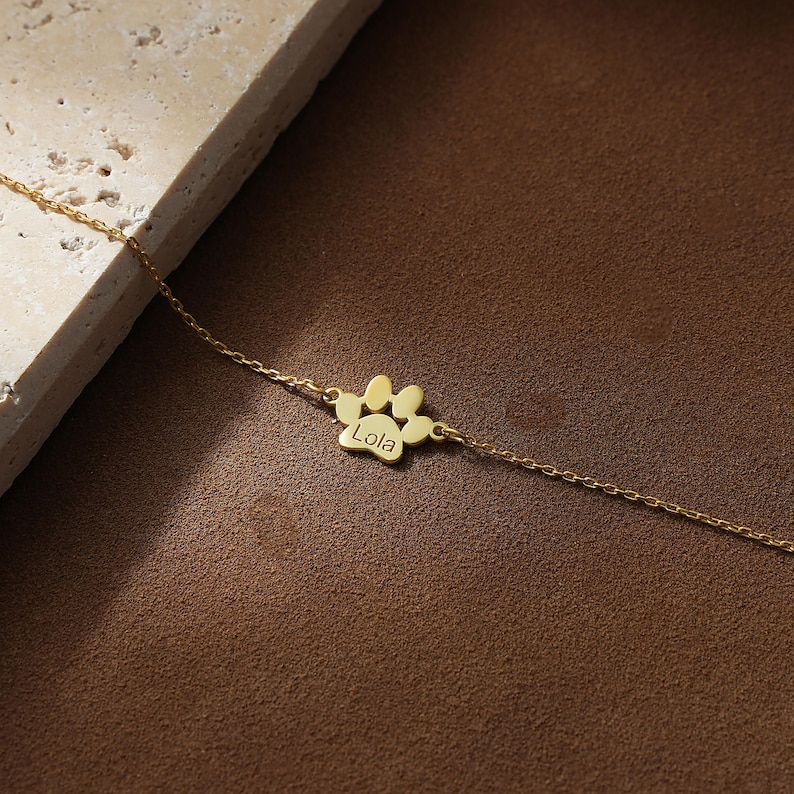 May include: A gold chain necklace with a paw print charm that says "Lola" on it.