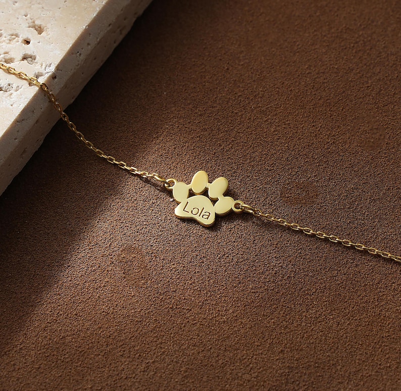 May include: A gold chain necklace with a paw print charm that says "Lola" on it.