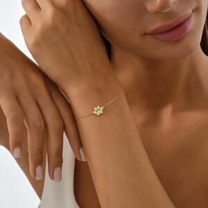 May include: A delicate gold chain bracelet with a small paw print charm. The bracelet is shown on a person's wrist.