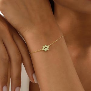 May include: A gold chain bracelet with a paw print charm. The charm has the name "Lola" engraved on it.