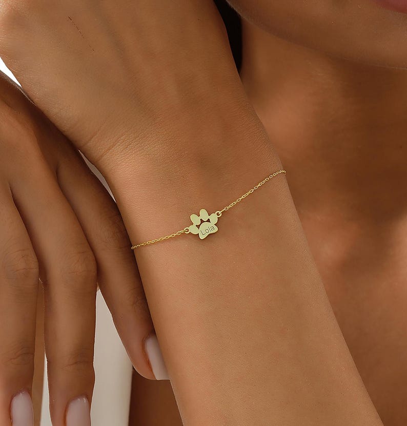 May include: A gold chain bracelet with a paw print charm. The charm has the name "Lola" engraved on it.