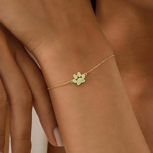 May include: A gold chain bracelet with a paw print charm engraved with the name "Lola".