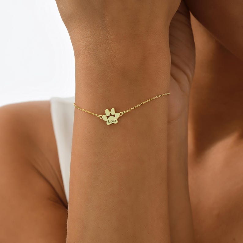 May include: Gold paw print charm bracelet with the name "Lola" engraved on the charm.