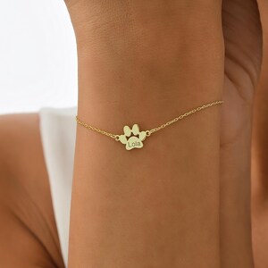 May include: Gold paw print charm bracelet with the name "Lola" engraved on the charm.