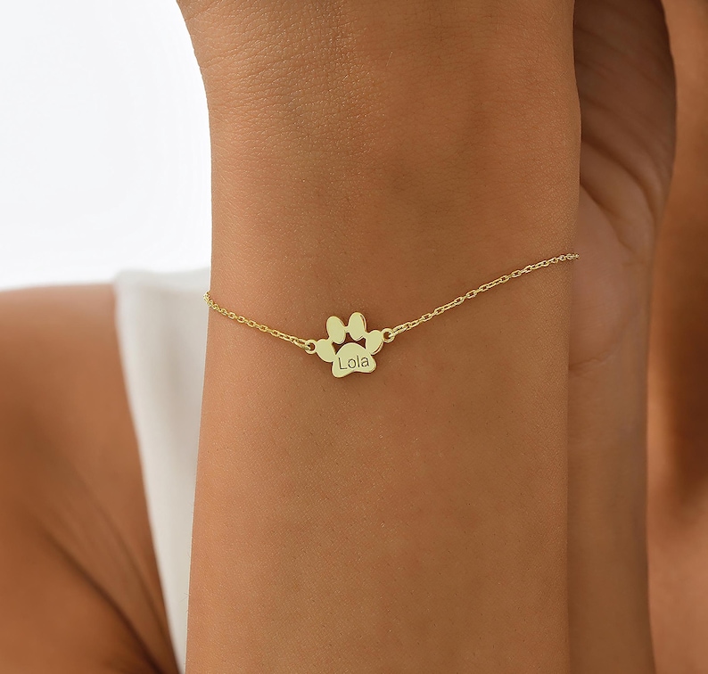 May include: Gold paw print charm bracelet with the name "Lola" engraved on the charm.
