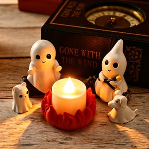 Peut inclure: Trois figurines de fantômes blancs, une petite figurine de chien blanc et une bougie LED à piles dans un support rouge en forme de lotus. La bougie émet une lueur chaude. Derrière les figurines se trouve un livre noir intitulé GONE WITH THE WIND.