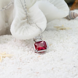 May include: A silver necklace with a red gemstone pendant shaped like a bottle. The pendant is set with small clear gemstones.