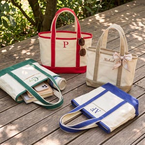 May include: Four canvas tote bags in red, green, beige, and blue. The red bag features the letter P, the beige bag has the name Michael and a ribbon, the green bag contains books and a phone, and the blue bag is embroidered with the letters AF.