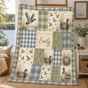 Peut inclure: Une courtepointe en patchwork sur le thème des canards avec des motifs à carreaux bleus et verts. Elle présente des illustrations de canards colverts dans l'eau, des roseaux et un nid. Le prénom Emily est inscrit au centre en écriture cursive.