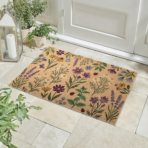 Può includere: Zerbino rettangolare con sfondo beige e motivo floreale. Il design presenta vari fiori nei toni del viola, bianco, giallo e blu, insieme a foglie verdi e piccole coccinelle rosse. Lo zerbino è posto davanti a una porta bianca.
