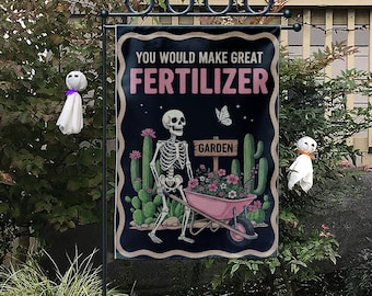 May include: A black garden flag with the text "YOU WOULD MAKE GREAT FERTILIZER" in pink. The flag features a skeleton pushing a pink wheelbarrow filled with flowers, with cacti and a butterfly.