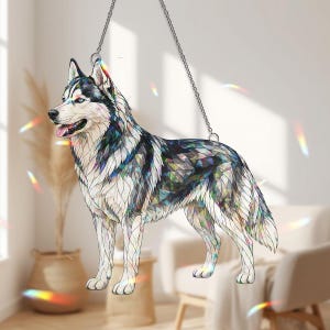 Può includere: Un ornamento decorativo a forma di cane husky, appeso a una catena. Il cane è raffigurato in stile vetrata, con un motivo a mosaico di blu, verdi e bianchi. Il cane ha gli occhi blu e la lingua rosa.