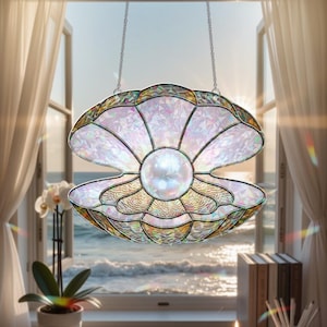 May include: A stained glass seashell suncatcher with a large pearl in the center, hanging in front of a window overlooking the ocean. The shell is iridescent with gold and pink accents, and is suspended by a silver chain.