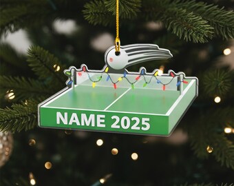 May include: A green and white table tennis ornament with the text "NAME 2025". The decoration features a net, colourful lights, and a ping pong bat design. It hangs from a gold string.