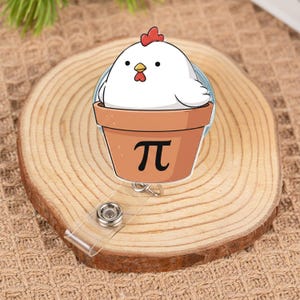 Könnte beinhalten: Ein klarer, runder, einziehbarer Ausweis-Rollenhalter mit einem Cartoon-Huhn in einem Terrakotta-Topf. Der Topf hat ein schwarzes "π"-Symbol. Das Huhn ist weiß mit rotem Kamm und Kehllappen.