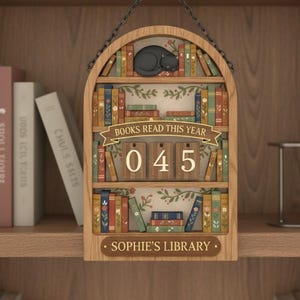 May include: Wooden bookshelf-shaped sign with a sleeping black cat on top. The sign reads "BOOKS READ THIS YEAR" above the number "045". The bottom of the sign says "SOPHIE'S LIBRARY". The sign is hanging from a chain.