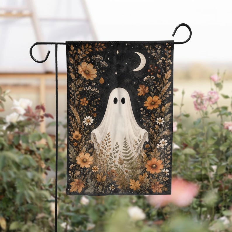 May include: A rectangular garden flag featuring a white ghost centered against a dark background. The ghost is surrounded by a border of orange and brown autumn flowers, ferns, and foliage. A crescent moon and small stars appear at the top.