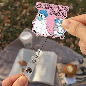 Może przedstawiać: Uchwyt na identyfikator z kreskówkowym duchem w masce chirurgicznej i czepku, z napisem "Spirited Sleep Service". Duch jest połączony z urządzeniem medycznym. Uchwyt jest przezroczysty z metalowym klipsem.