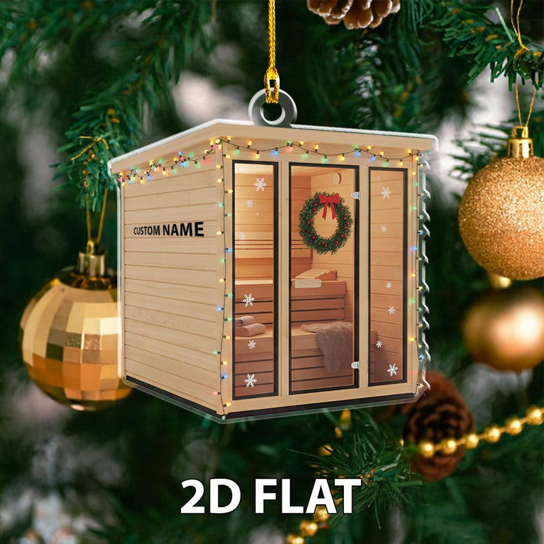 May include: A 2D flat Christmas ornament shaped like a sauna, with the text "CUSTOM NAME" and "2D FLAT". The sauna features a wreath, snowflake details, and string lights. The ornament hangs from a gold string.