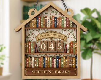 May include: Wooden bookshelf-shaped sign with a house-like top, hanging by a chain. The sign features a floral wallpaper background and two shelves filled with colorful, decorative books. The text "BOOKS READ THIS YEAR" is on a banner, and the number "045" is displayed. The bottom reads "SOPHIE'S LIBRARY."
