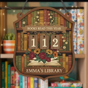 May include: Wooden sign with a bookshelf design, featuring the text "BOOKS READ THIS YEAR" and the numbers "112". The sign also includes the text "EMMA'S LIBRARY" and a floral arrangement.