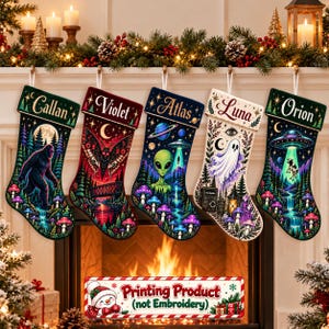 Könnte beinhalten: Fünf Weihnachtssocken hängen in einer Reihe, jede mit einzigartigen Grafikdrucken von Bigfoot, einem Nachtfalter, einem Alien, einem Geist und einem UFO, das eine Kuh entführt. Jede Socke ist mit den Namen Callan, Violet, Atlas, Luna und Orion personalisiert.