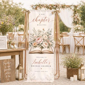 May include: A vertical fabric banner on a copper stand featuring the text A NEW CHAPTER BEGINS, a floral illustration emerging from an open book, and the text WELCOME TO Isabelle's BRIDAL SHOWER AUGUST 24TH 2026, accented with beige ribbons.