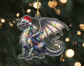 May include: A dragon-shaped Christmas ornament with a Santa hat and string lights. The dragon is silver and gray with intricate details. The ornament has the text "NAME" on the hat and "2D FLAT" at the bottom.